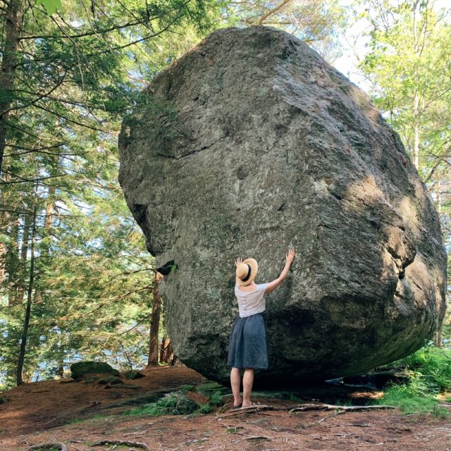 Woman touching huge balanced rock in forest